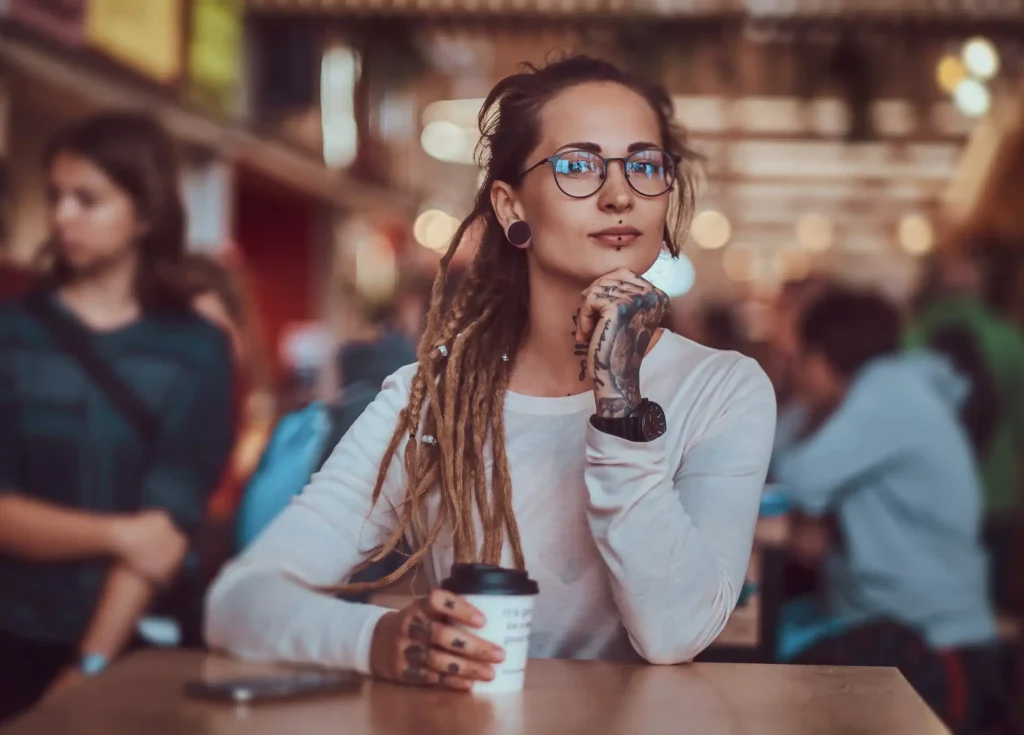 beautiful-cheerful-girl-with-tattooes-dreadlocks-is-sitting-food-court-while-drinking-coffee